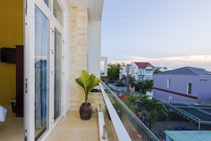 A balcony with a potted plant, a glass door, and a view of neighboring houses. - Hoi An Green Town House Homestay (Da Nang)