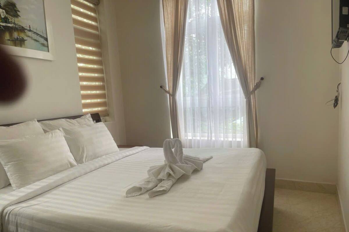 A neatly made bed with white linens and a towel arranged in a swan shape on the bed.