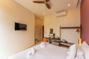 Ein Hotelzimmer mit Bett, Schreibtisch, Fernseher und Deckenventilator.