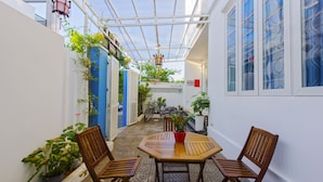 A covered patio with a wooden table and chairs, surrounded by potted plants and a bicycle. - Hoi An Green Town House Homestay (Da Nang)