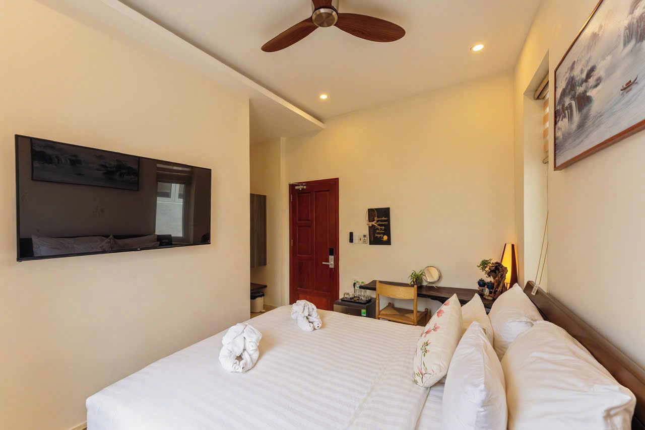 A hotel room with a bed, a ceiling fan, a painting, and a door.
