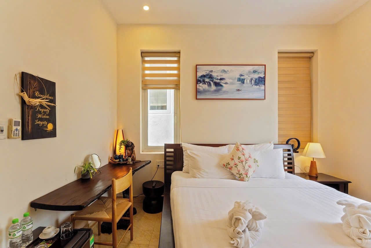 A hotel room with a bed, bedside table, lamp, and a painting on the wall.