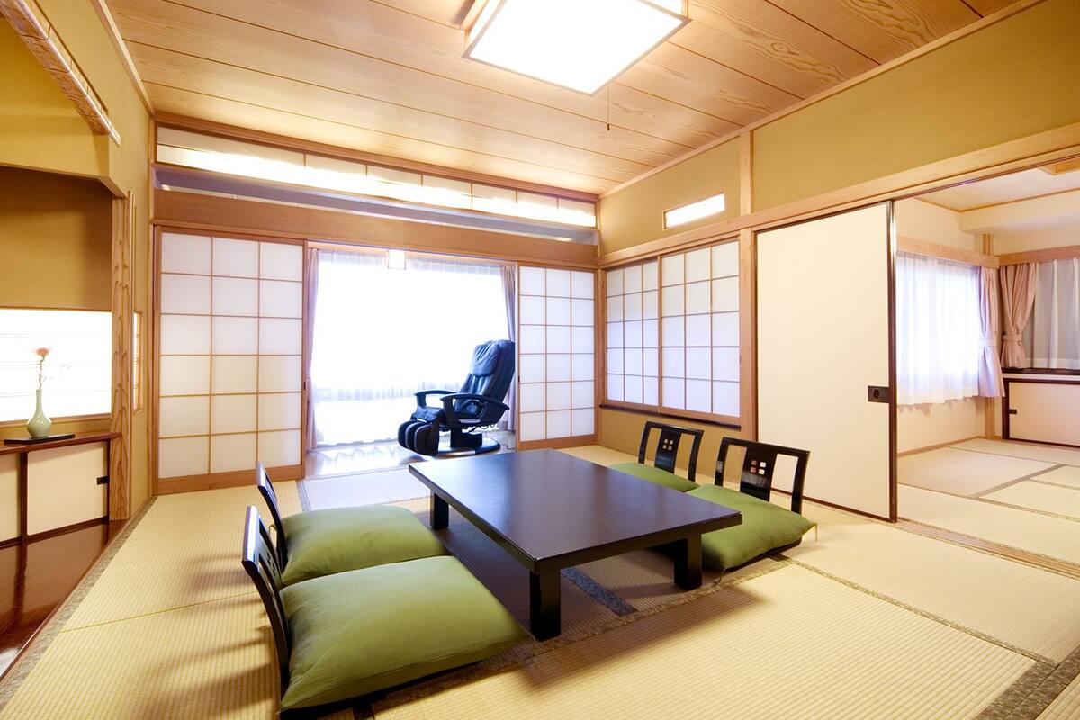 A traditional Japanese room with tatami flooring, a low table, green cushions, a black chair, and sliding doors.