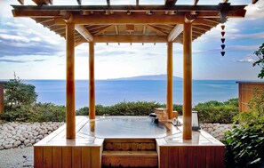 Una pérgola de madera con hidromasaje y vistas al mar.