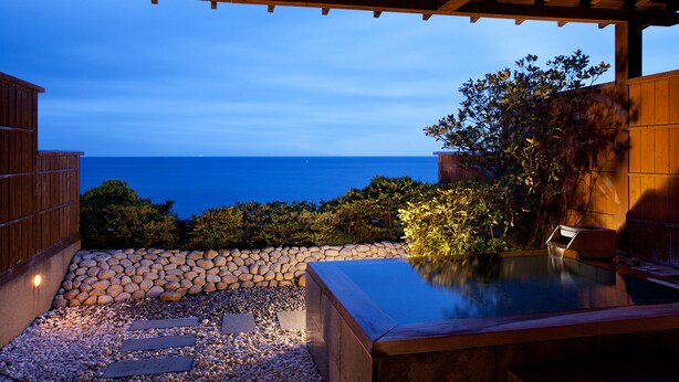 Een terras met een stenen pad, een houten pergola en uitzicht op de oceaan.