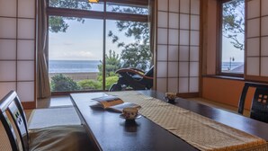 Een traditionele Japanse kamer met tatami vloerbedekking, een lage tafel met een boek en een kop, en grote ramen met uitzicht op de zee.