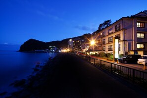 Un hotel frente al mar con un paseo marítimo empedrado, varios pisos e iluminación en la calle.