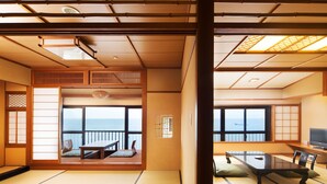 Een traditionele Japanse kamer met tatami vloeren, een schuifdeur naar een balkon met uitzicht op zee, en een televisie aan de rechterkant.