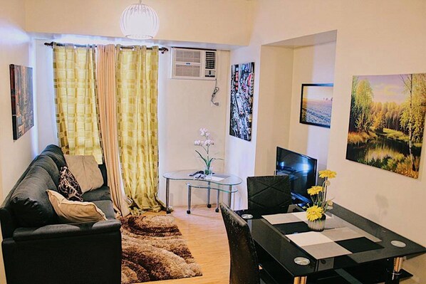 A living room with a sofa, a glass coffee table, a TV, and artwork on the walls. - 1BR Condominium at Avida Towers Cebu IT Park (Cebu City)