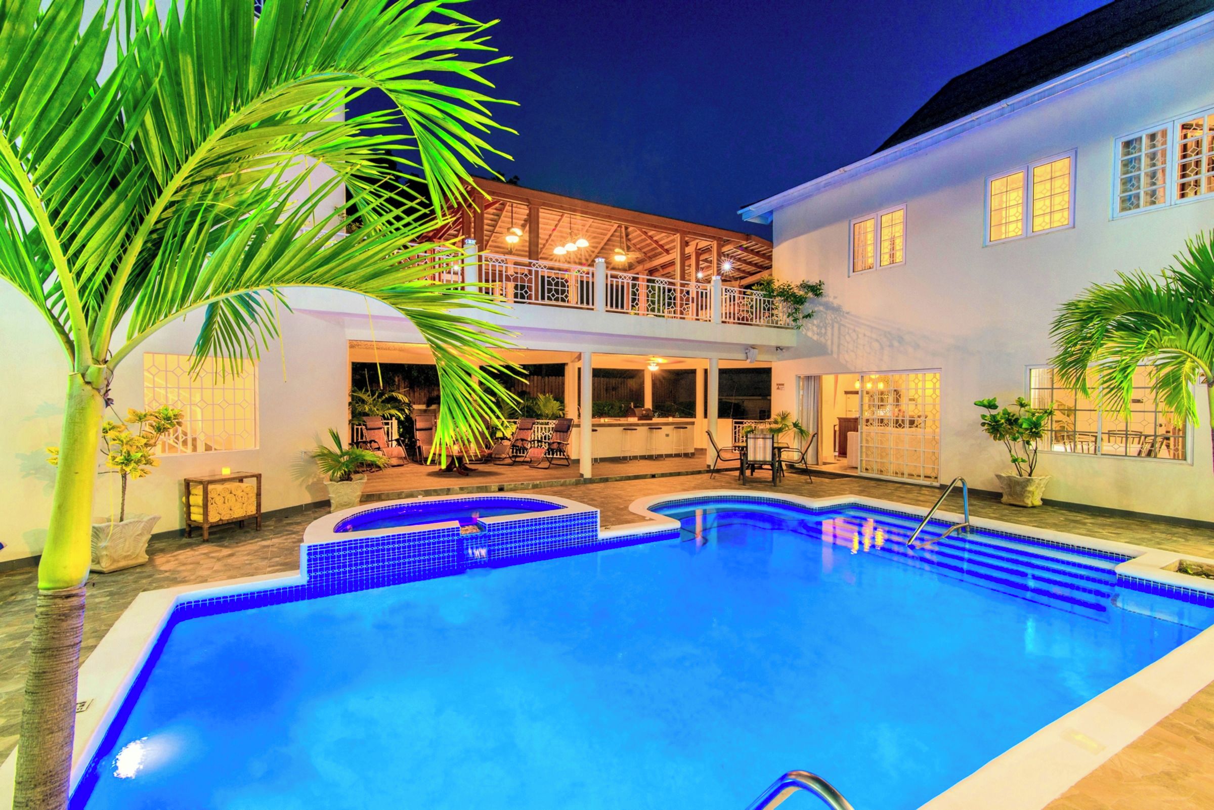 Una piscina con zona de estar hundida, rodeada por un porche cubierto con mobiliario de exterior.