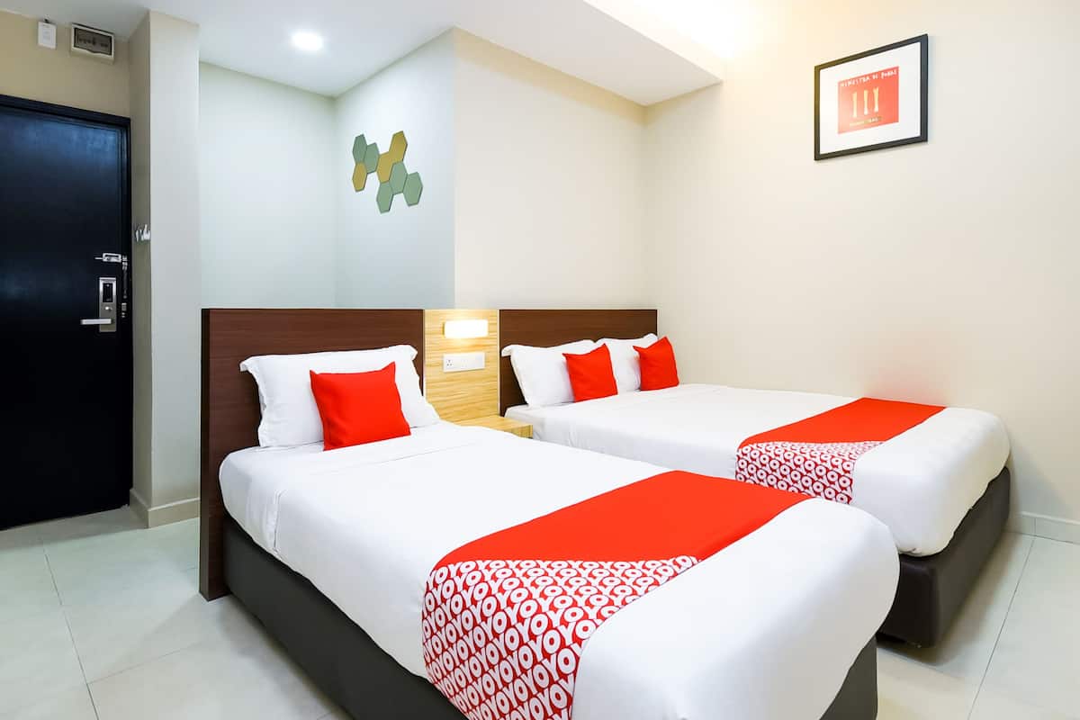 A hotel room with two beds, a black door, a wall-mounted light, and a framed picture.