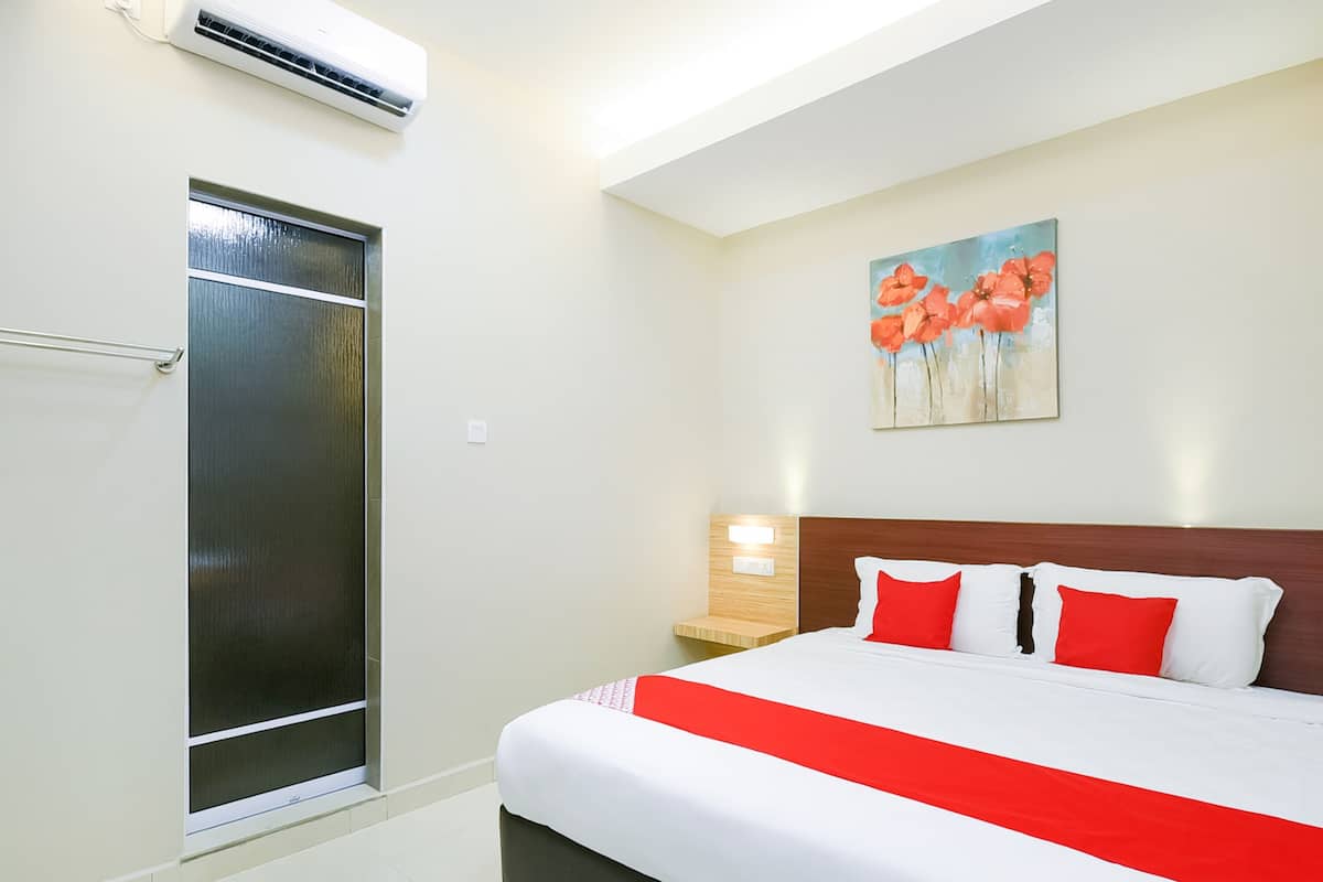 A hotel room with a bed, a nightstand, a painting, and an air conditioning unit.