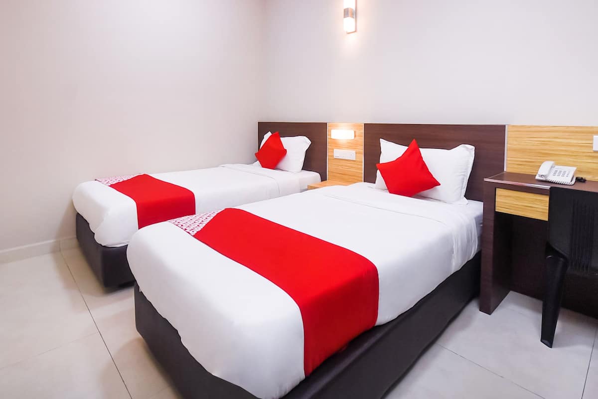 A hotel room with two beds, each with white bedding and red accents, a wooden headboard, a bedside table with a phone, and a wall-mounted light.