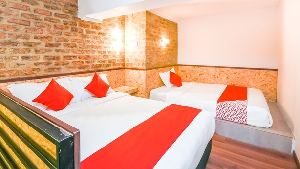 Une chambre d’hôtel avec deux lits, chacun recouvert d’une literie rouge et blanche, et un mur en briques.