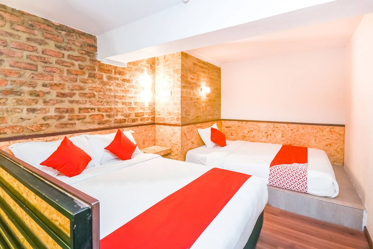 A hotel room with two beds, each with red and white bedding, and a brick wall.