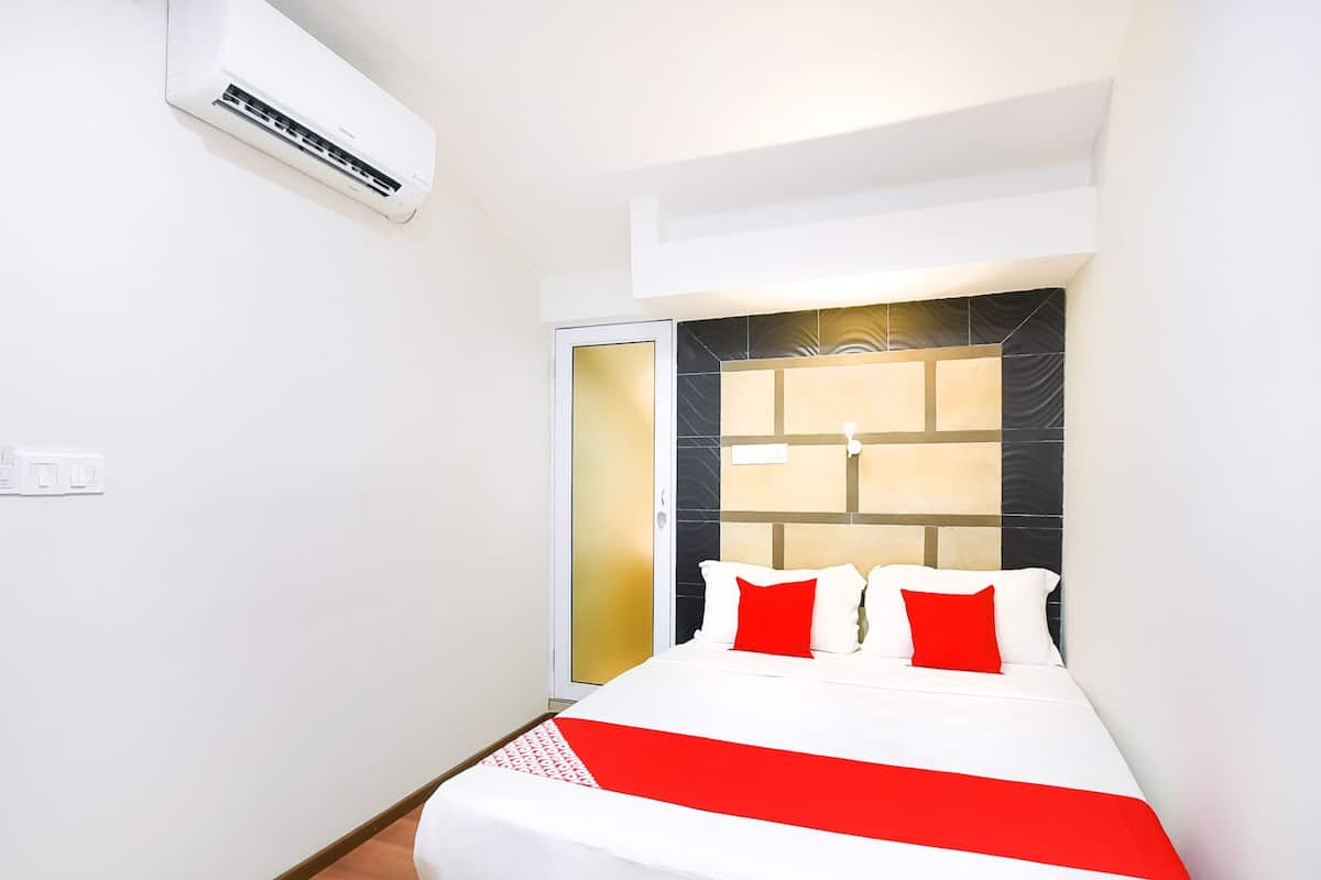 A hotel room with a bed, a window, an air conditioning unit, and a door.
