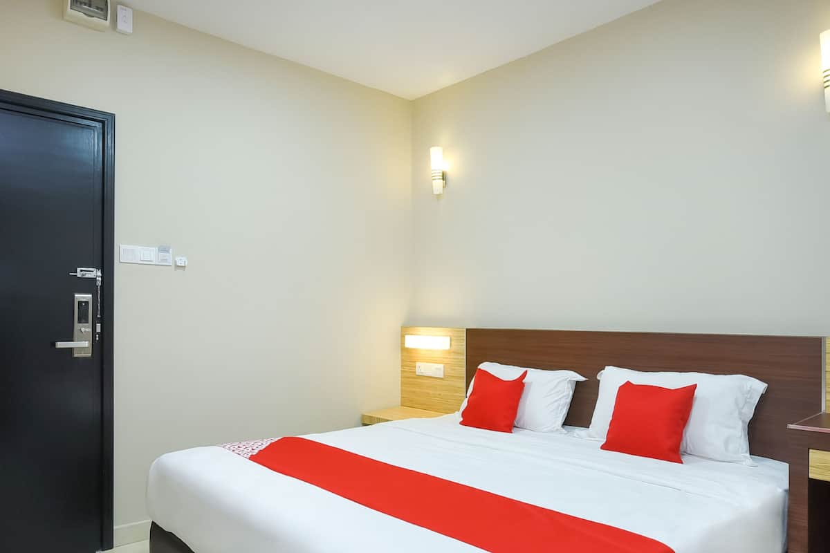 A hotel room with a bed, a wooden headboard, a nightstand, a wall-mounted light, and a door with a lock.