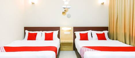 Habitación de hotel con dos camas, cada una con ropa de cama blanca y detalles rojos, cabeceros de madera y una lámpara de pared.