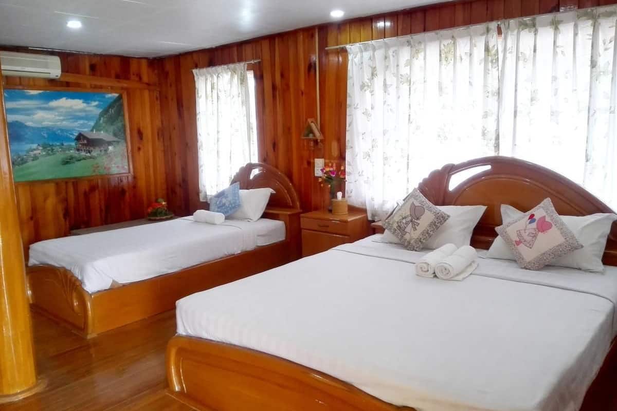 Una habitación de hotel con dos camas de madera, cabeceros de madera, una mesita de noche, una lámpara y un cuadro en la pared.