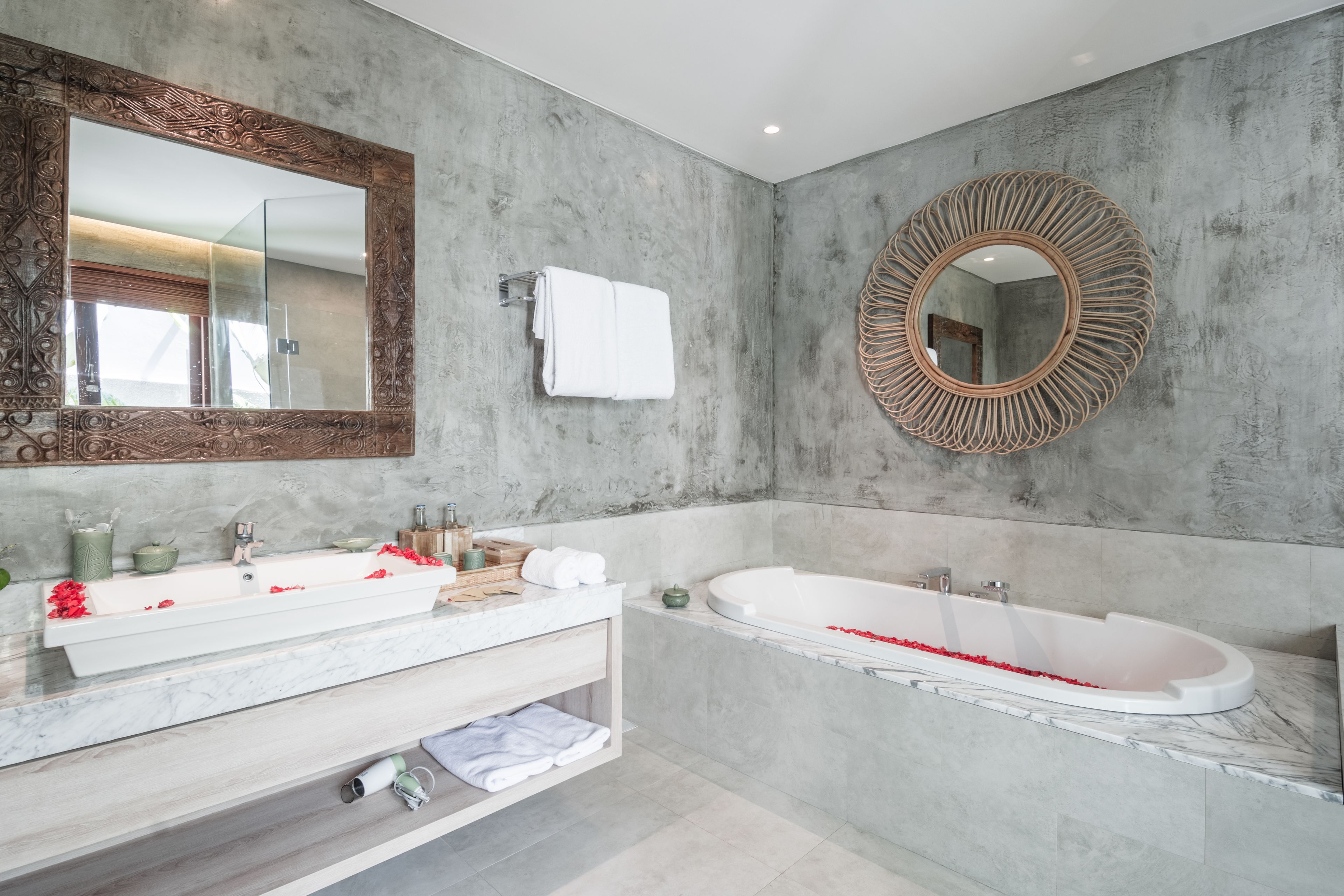 A modern bathroom with a large mirror, a bathtub, and a vanity with a marble countertop.