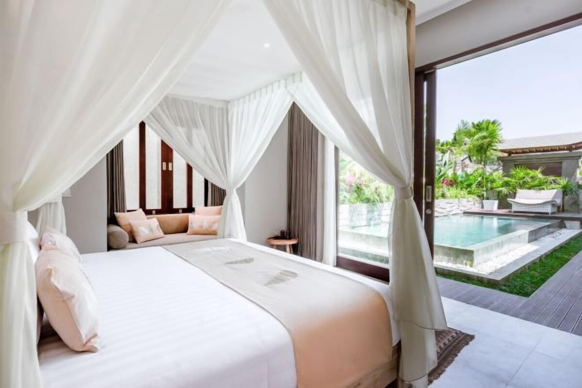 A bedroom with a large bed, a view of a swimming pool, and a balcony.