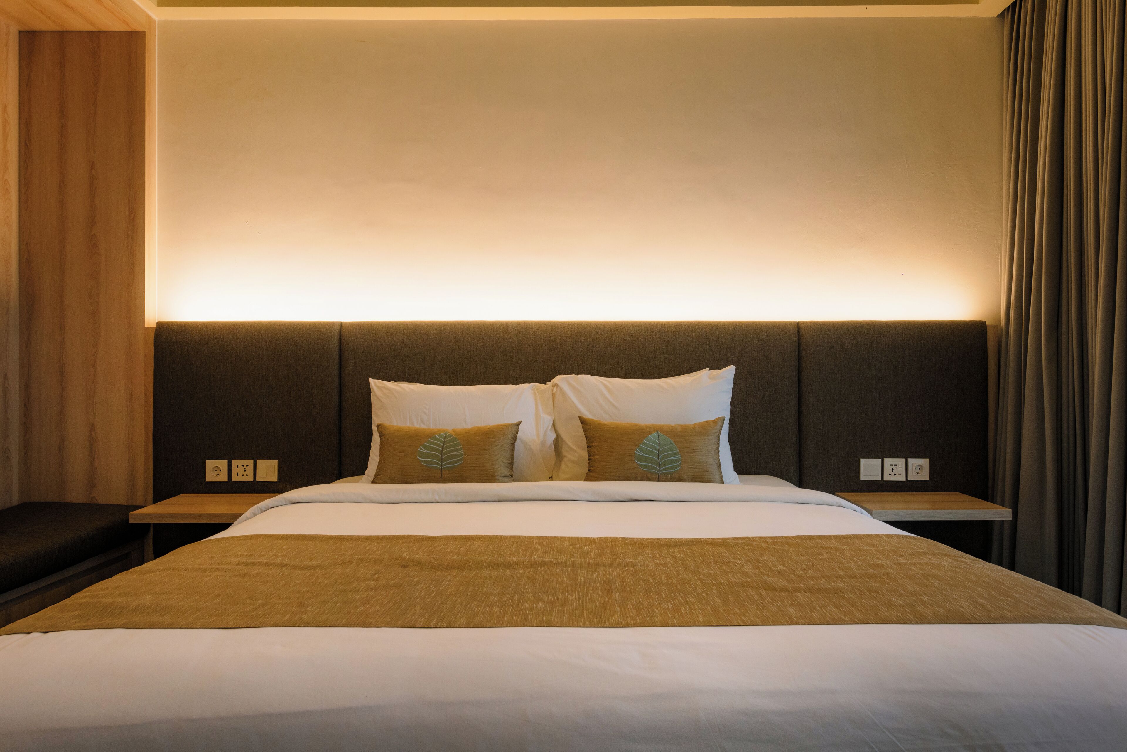 Una habitación de hotel con una cama grande, dos mesitas de noche y un cabecero con iluminación integrada.
