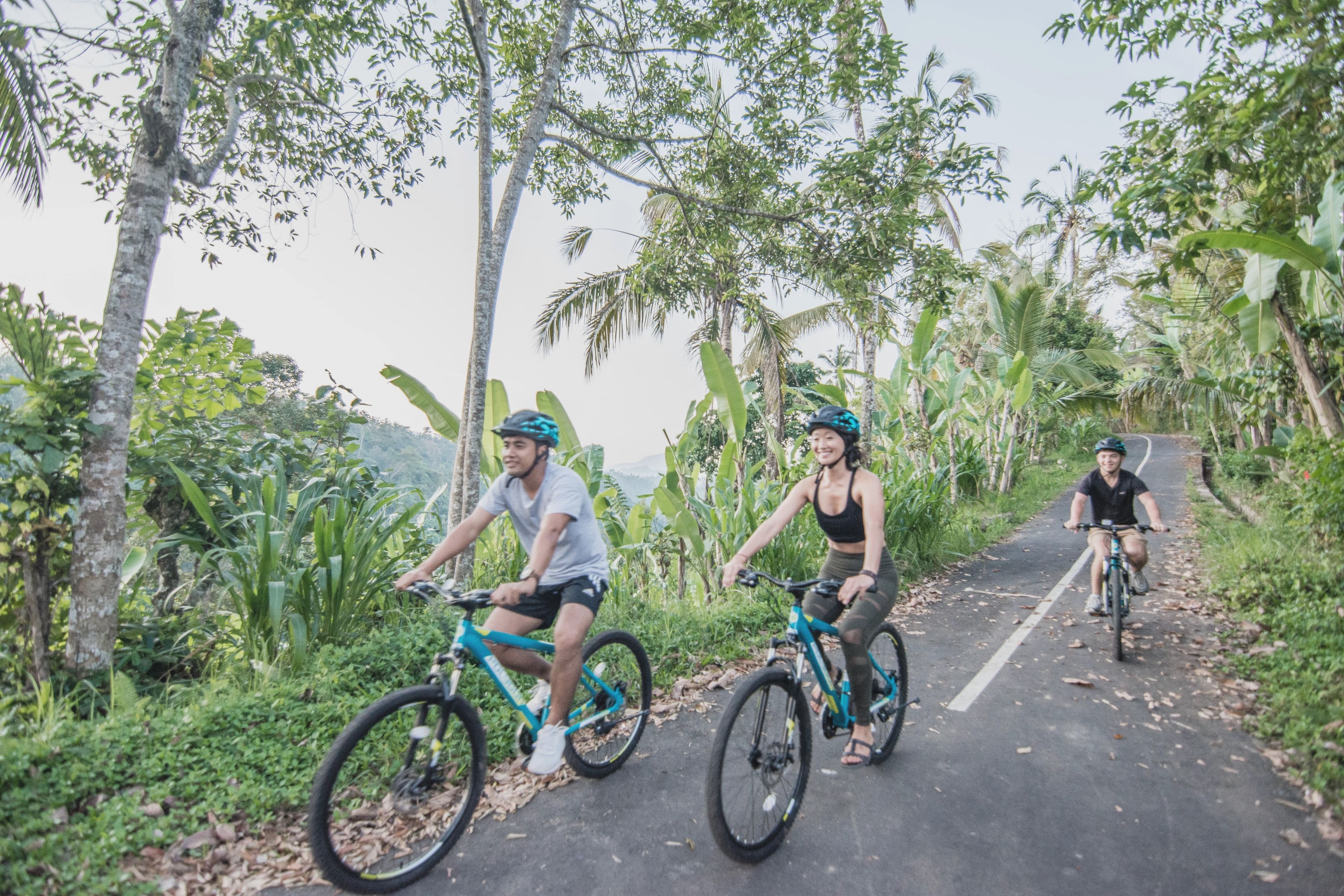 Three people riding bicycles on a paved path surrounded by lush greenery and trees.