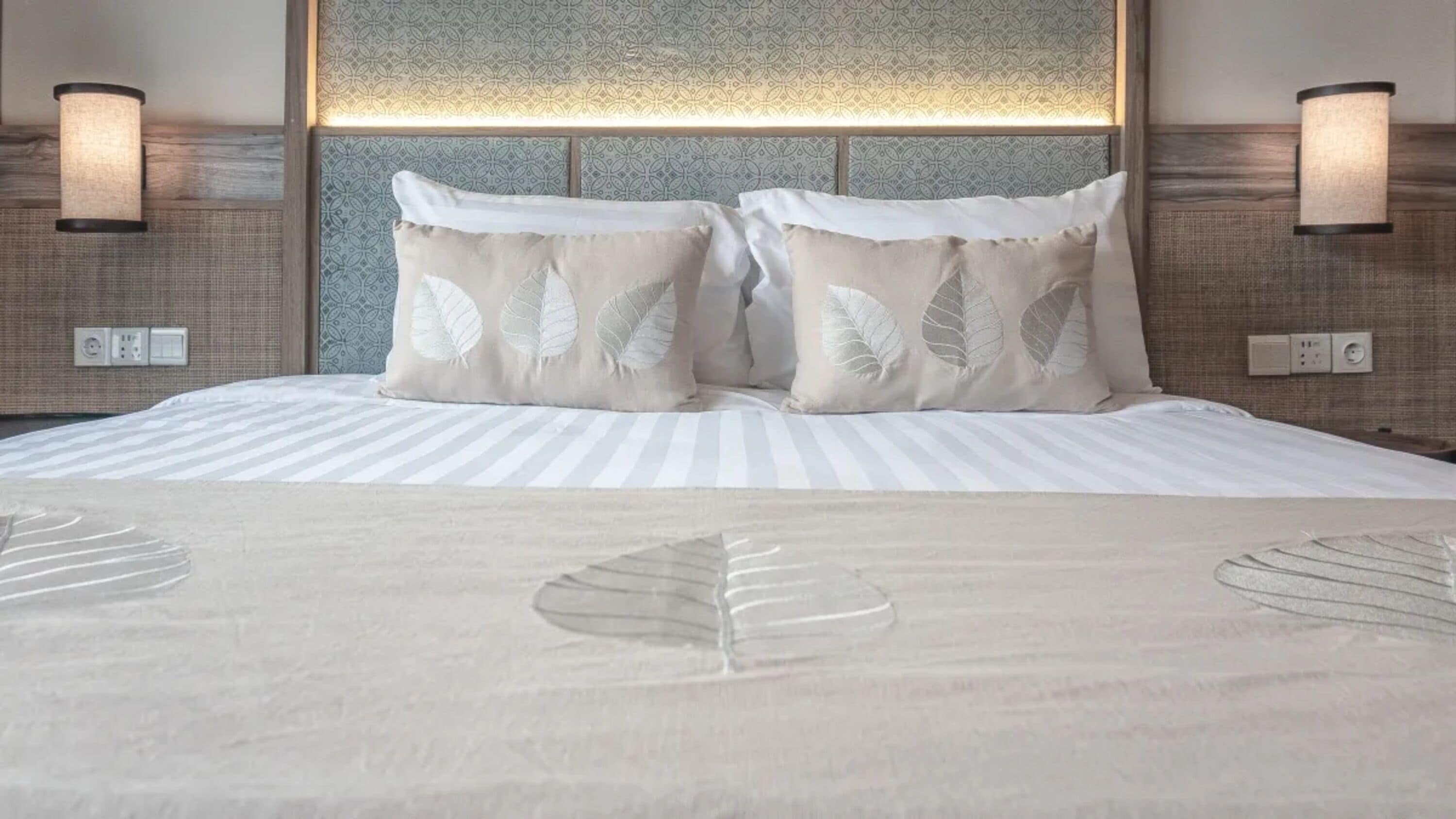 A hotel room with a bed, two wall-mounted lamps, and a patterned headboard.