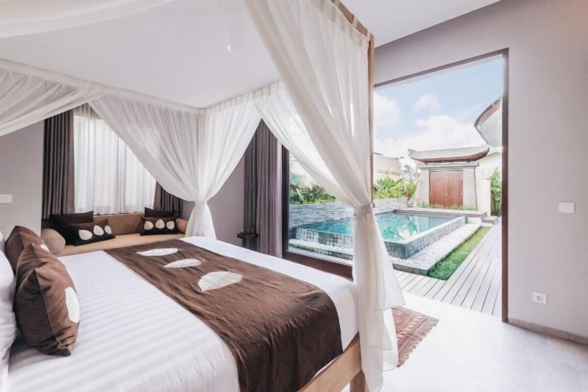 A bedroom with a large bed, a canopy, and a view of a swimming pool.