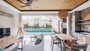 A modern living room with a pool view, wooden furniture, and a ceiling fan. - Daun Lebar Villas (Payangan)