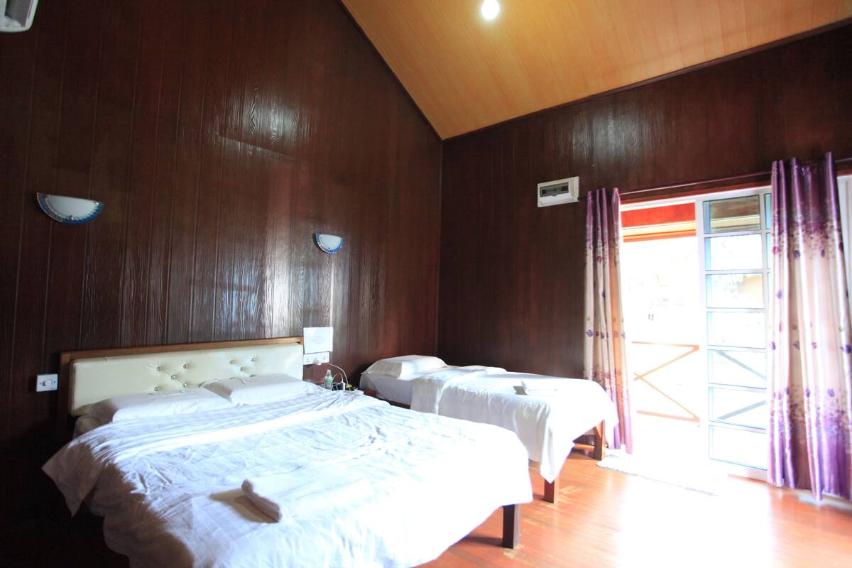 Habitación de hotel con dos camas, paredes de madera, una lámpara en el techo y una ventana con cortinas.