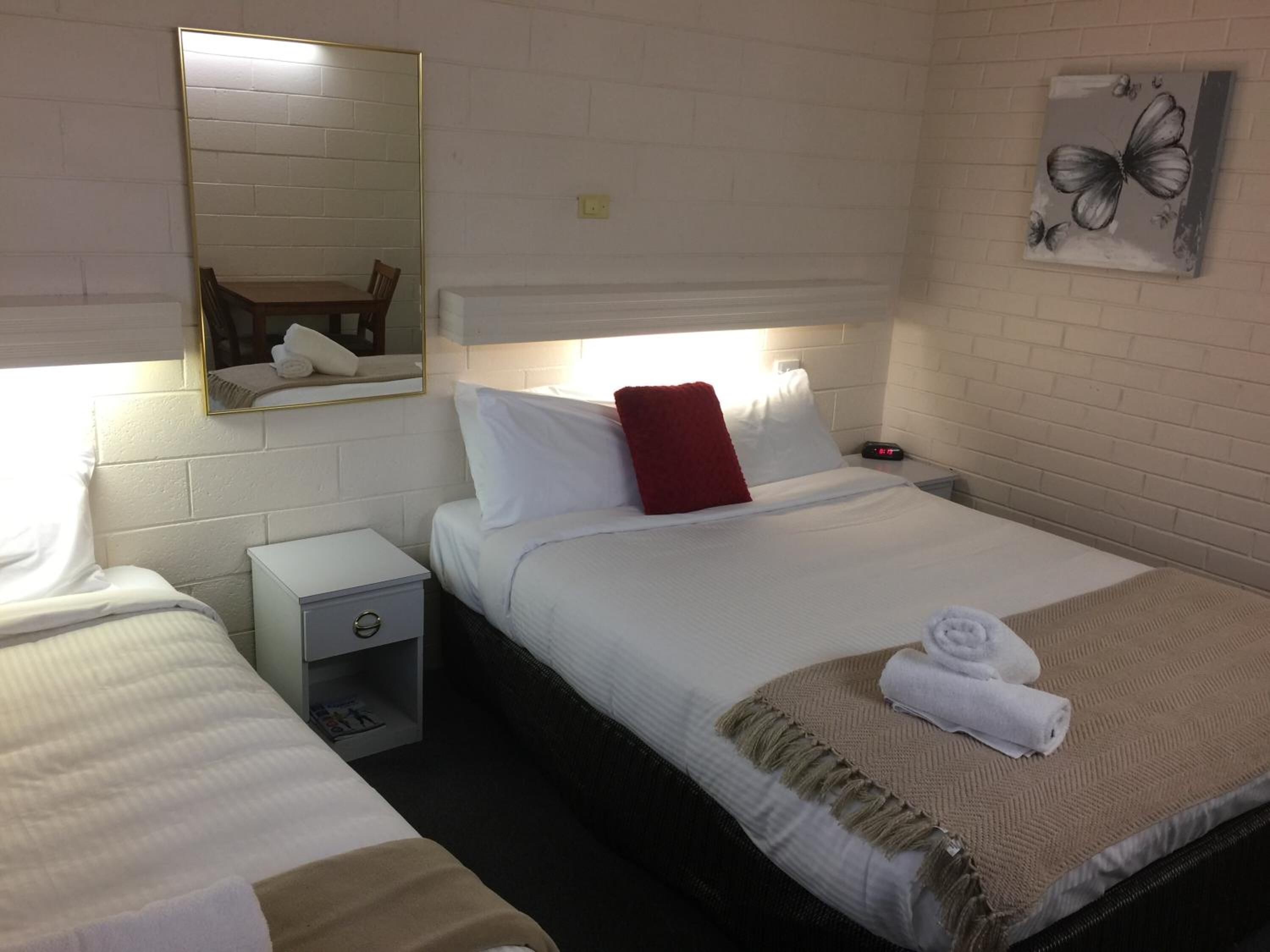 Et hotelværelse med to senge, et natbord med lampe, en lille kommode og et spejl på væggen.