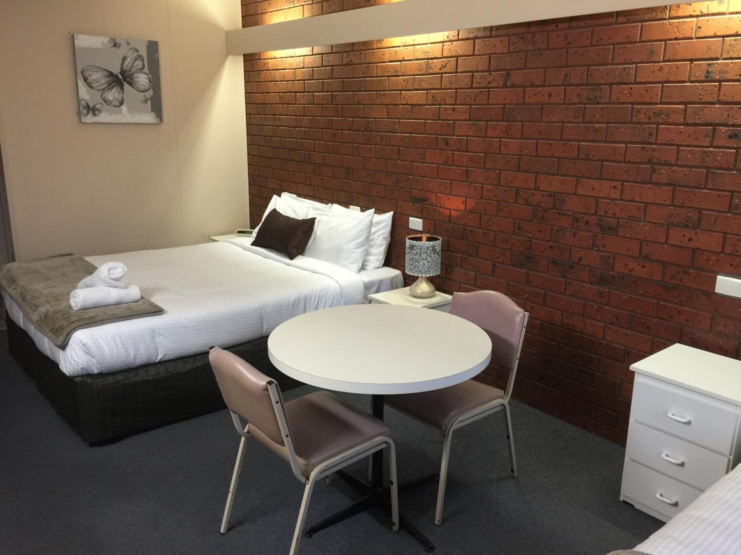 A hotel room with a bed, two chairs, a round table, a nightstand, and a dresser.