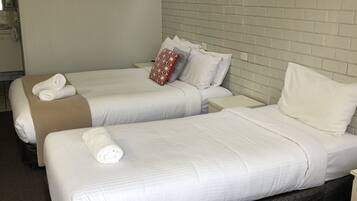 Habitación de hotel con dos camas, ropa de cama blanca, un cuadro de una flor roja en la pared y un cabecero con estampado de ladrillo.