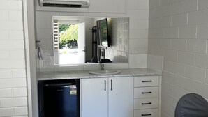 A compact kitchen with a built-in sink, a small refrigerator, and a window with a view of greenery. - Wattle Motel (Seymour)