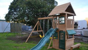 A wooden play structure with a slide and swings in a backyard. - Wattle Motel (Seymour)