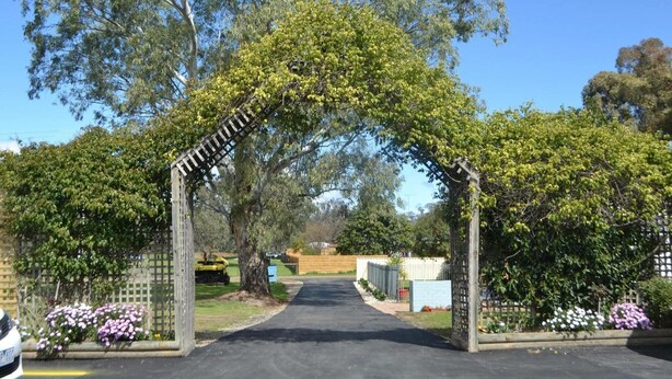 A pathway leading through a garden with a wooden archway, surrounded by trees and flowering plants. - Wattle Motel (Seymour)