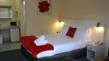 A hotel room with a bed, bedside table, and a desk with a microwave.
