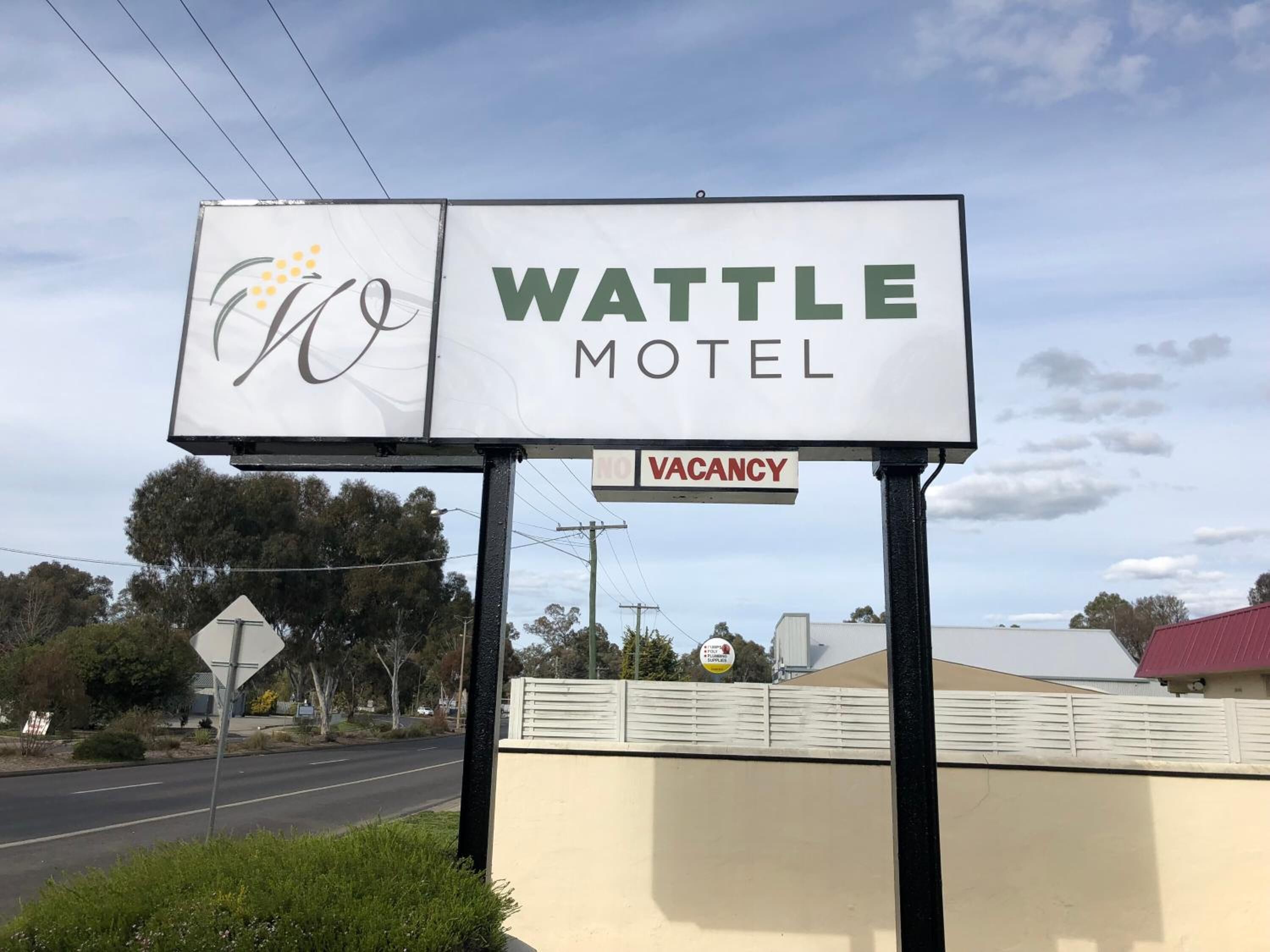 Señal de motel con el nombre "WATTLE MOTEL" y un letrero que indica "HABITACIONES DISPONIBLES" debajo.