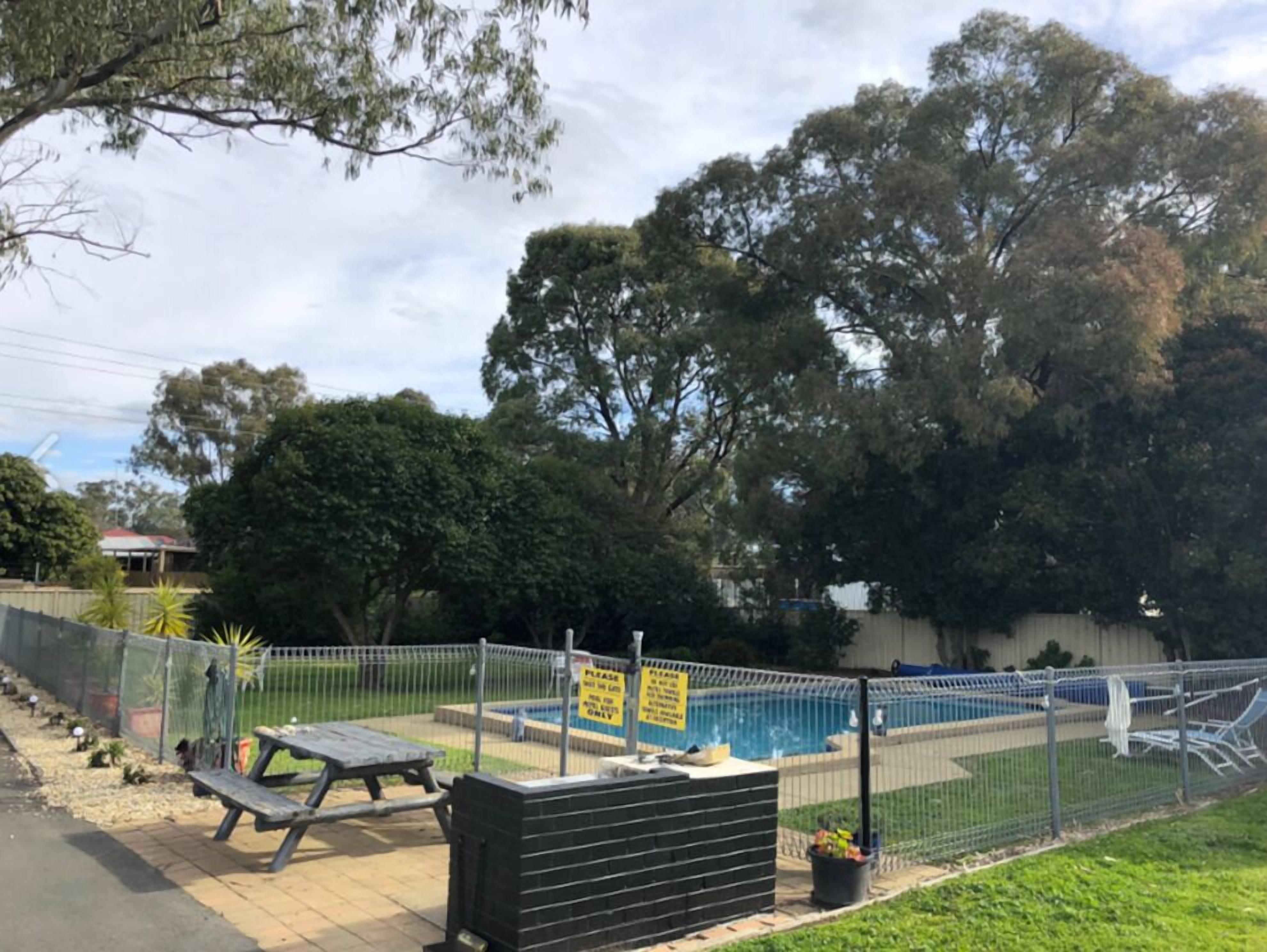 A fenced outdoor area with a pool, picnic tables, and a sign indicating no swimming.