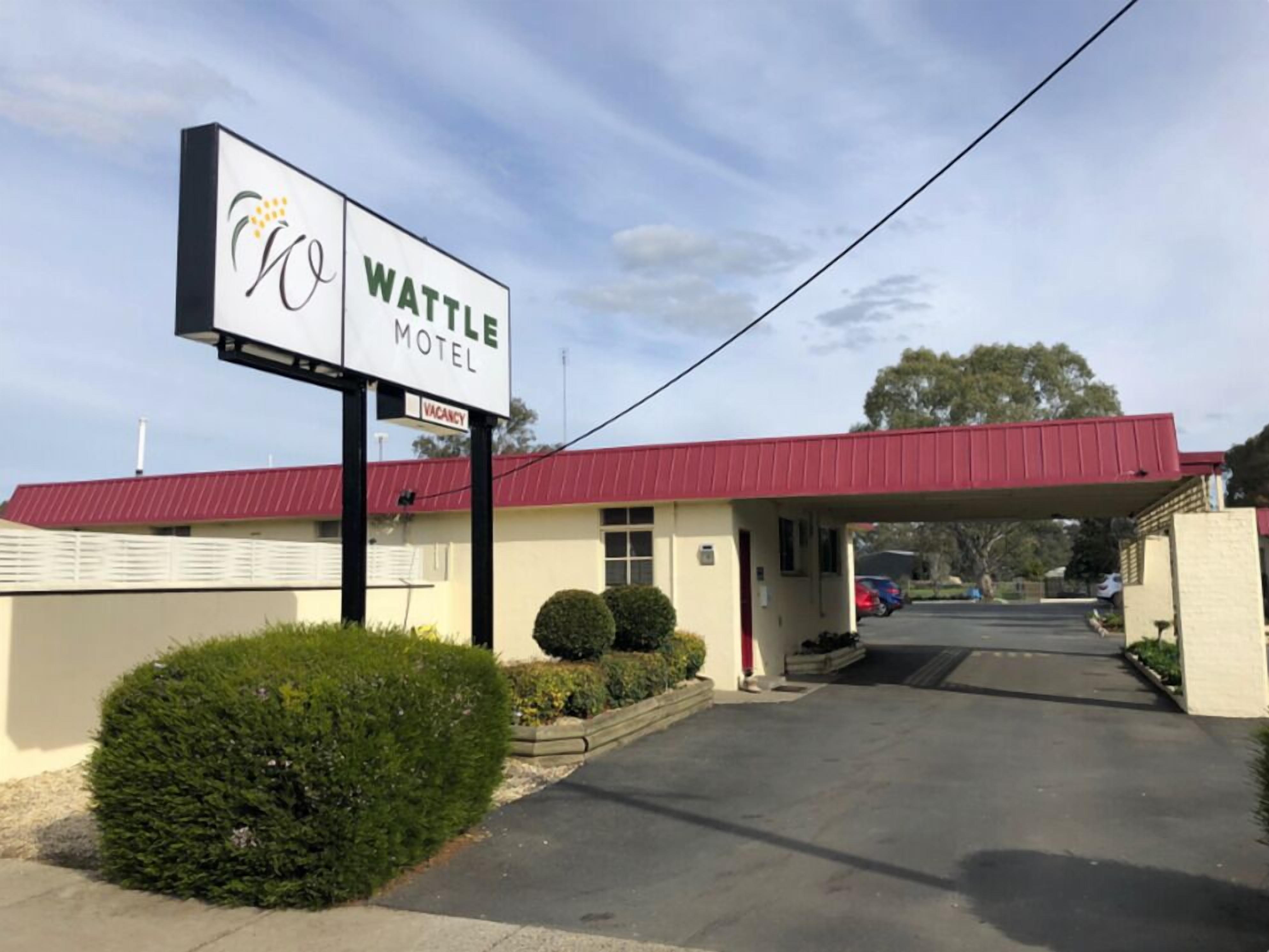 Un motel Wattle con techo rojo, un letrero y una entrada pavimentada.
