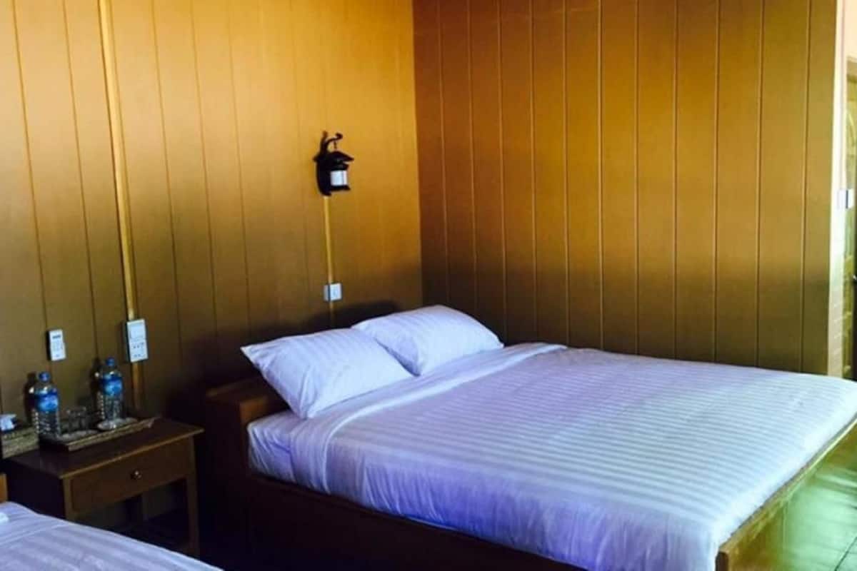 A hotel room with two beds, wooden panel walls, a nightstand with a lamp, and a window with curtains.