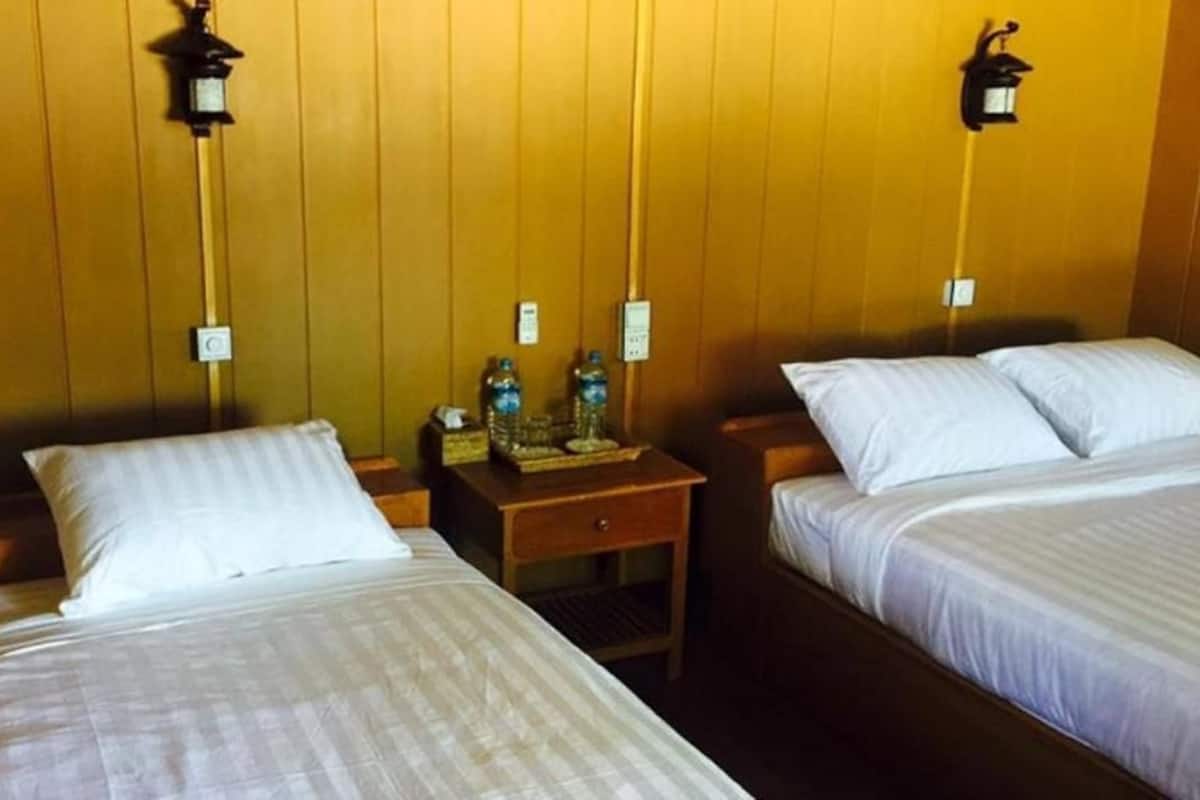 A room with two beds, wooden walls, and wall-mounted lamps.
