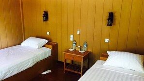 A hotel room with two single beds, wooden walls, a small wooden nightstand with a lamp, and a water bottle on the nightstand. - Golden Fish Motel (Nyaungshwe)