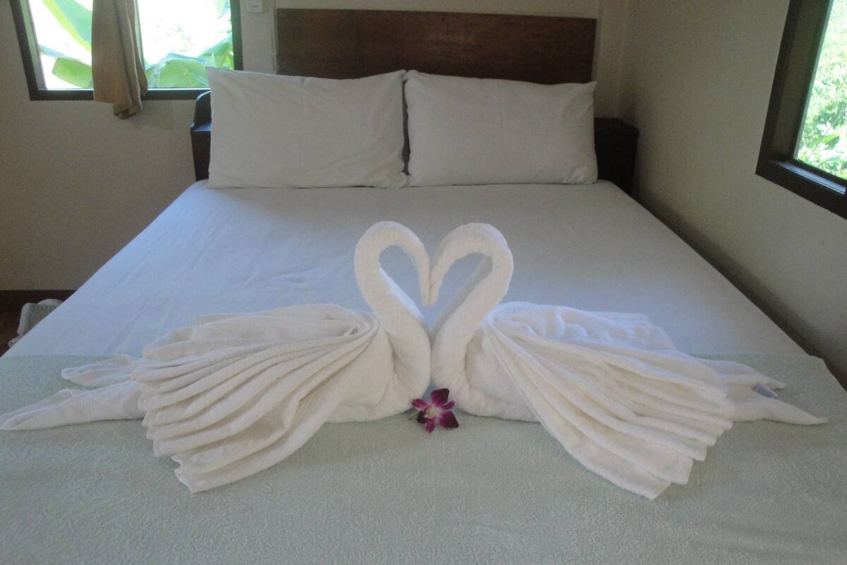 A bed with a towel arrangement in the shape of two swans and a purple flower.