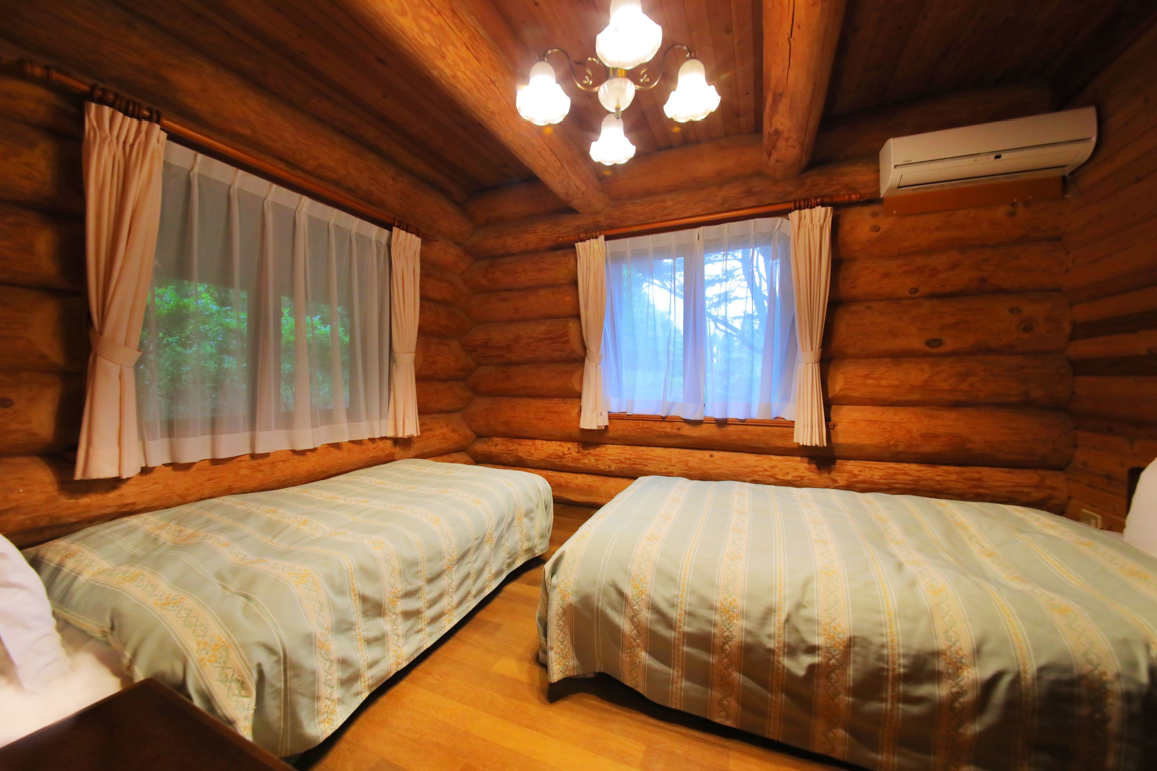 A log cabin room with two beds, wooden walls, and a chandelier.