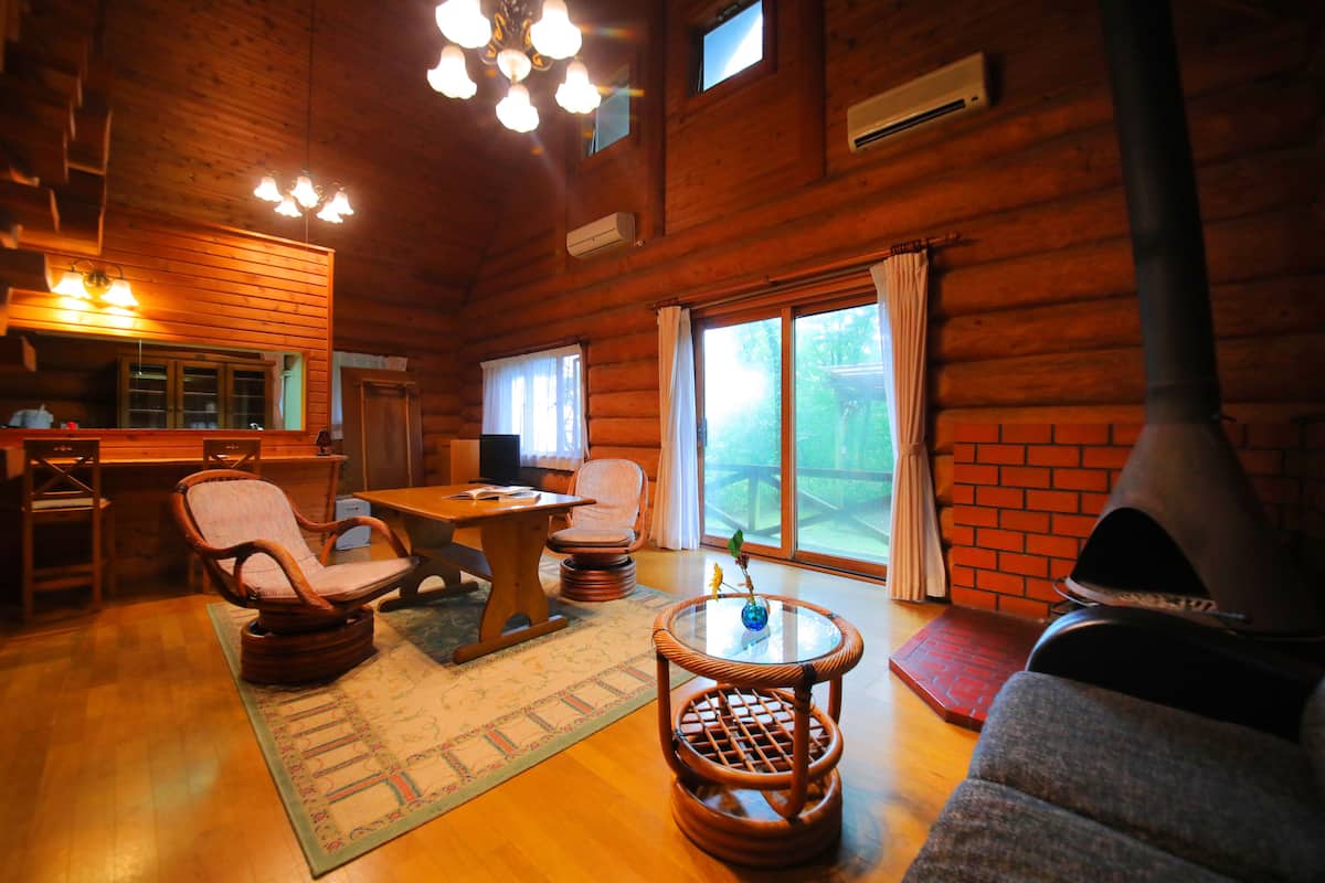 Interior acolhedor de uma cabana de madeira, com área de jantar, móveis de vime, lareira e janelas amplas.