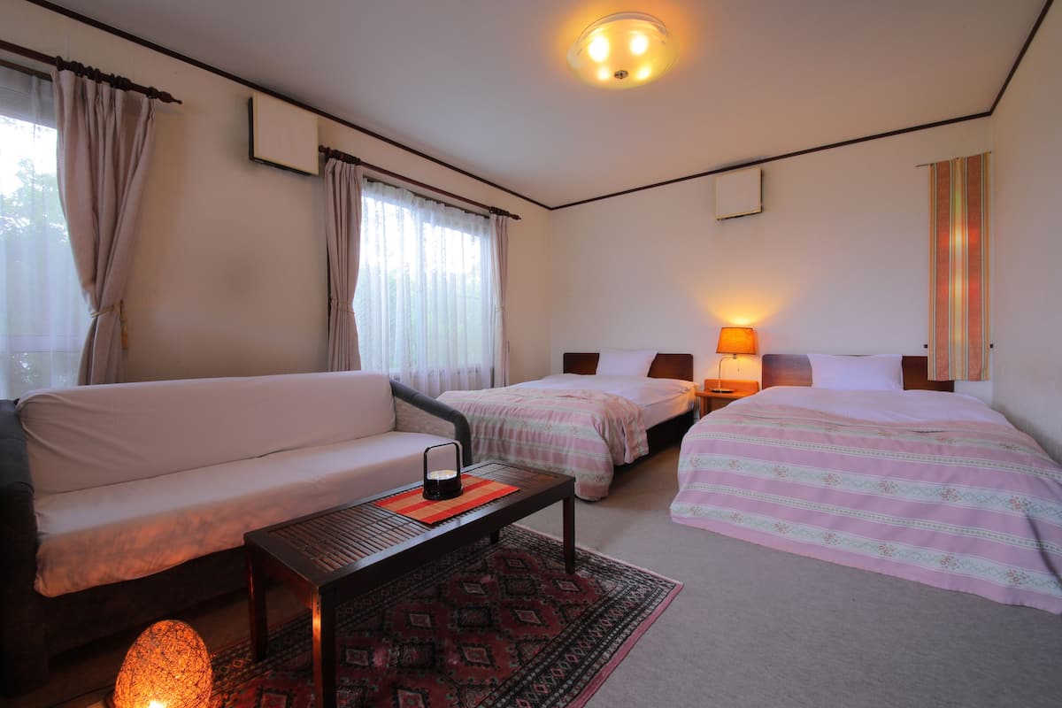 Quarto de hotel com sofá, duas camas, mesa de cabeceira com abajur e tapete estampado.