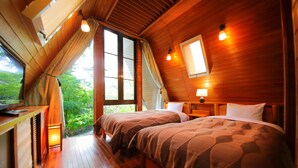 Un dormitorio de cabaña de madera con dos camas, un escritorio pequeño y una ventana con vistas a la vegetación.