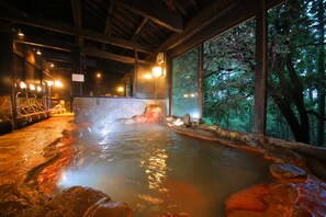 A hot spring area with a wooden interior, stone seating, and a view of the forest through large windows.